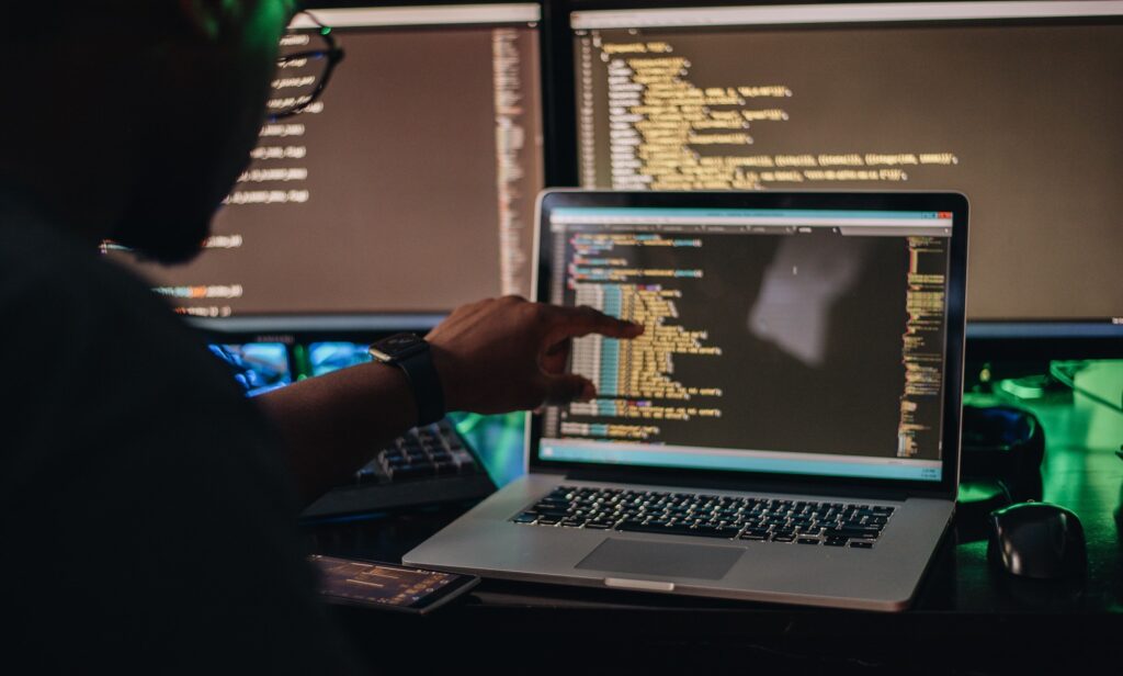 African American man sitting at computer desk looking at computer code, programming, developer